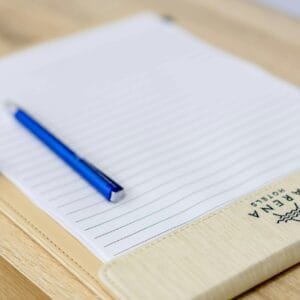 A blue pen rests on a lined notebook placed on a wooden desk, ideal for writing or hotel stationery themes.