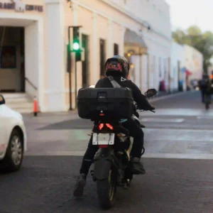 imagen-repartidor-moto-delivery-optimizado-ats Repartidor de delivery con mochila de transporte en moto circulando por una zona urbana de Tenerife.